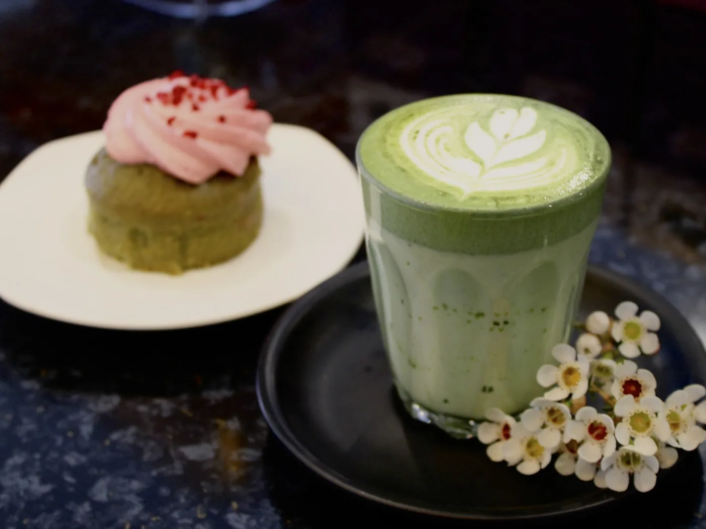 A matcha strawberry cake on a plate, next to a matcha latte